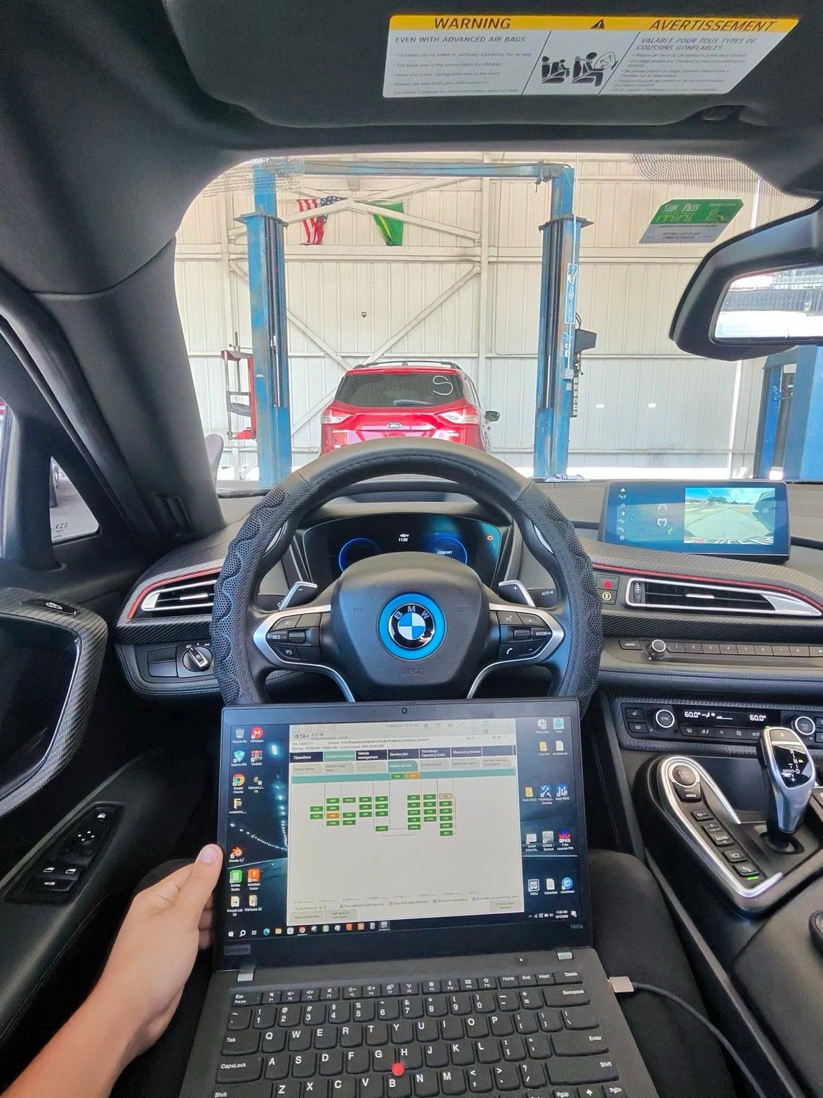 Laptop running BMW ISTA diagnostic software inside a BMW during a diagnostic session
