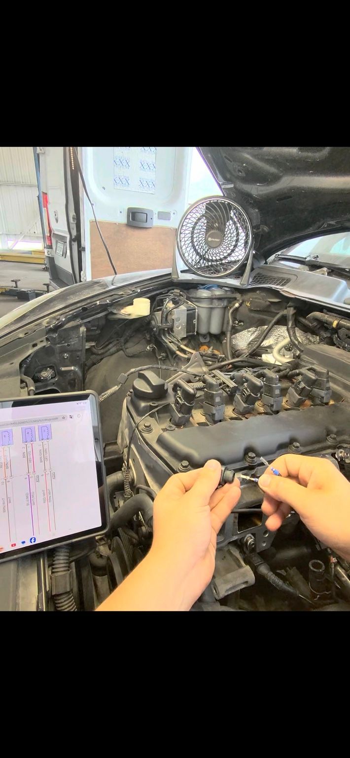 Technician testing an ignition coil connector on an engine while following a wiring diagram on a tablet